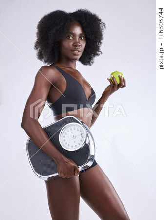 Fitness, scale and black woman portrait with apple in studio for wellness, gut health and diet, detox or balance on white background. Body, care and model with organic, fruit or weight loss progress 116303744