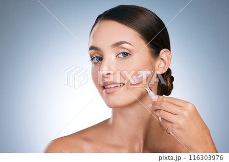 Portrait, woman and skincare for beauty with face roller, satisfied and results for glowing skin in blue background. Female person, studio and cosmetic product with pride, dermatology for wellness 116303976