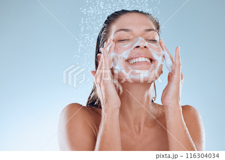 Woman, facial and soap for skincare hygiene with foam, wash or clean against blue studio background. Happy, splash and model person for body wellness, cosmetics or healthy skin treatment in water 116304034