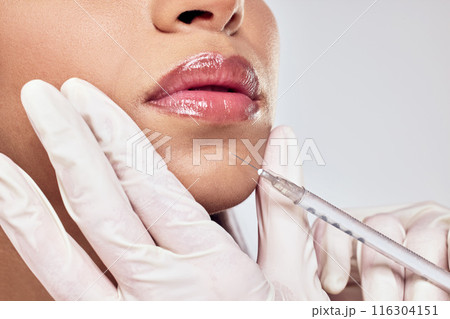 Hands, injection and woman lips for plastic surgery with beauty transformation and cosmetic procedure in studio. Surgeon needle, patient mouth and liquid collagen for anti aging by grey background 116304151