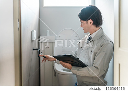 トイレのタオルハンガーをチェックする水道屋・設備屋の作業着姿の男性 116304416