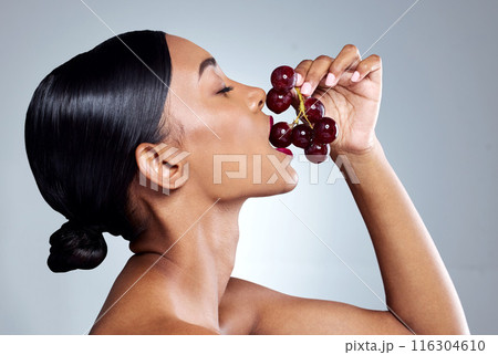 Hungry, woman and grapes in mouth for wellness, vegan diet or healthy eating in grey studio background. Nutrition, organic food and female person with fruit isolated against backdrop for self care 116304610
