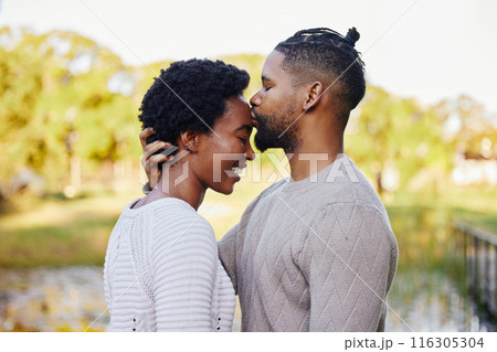 Black couple, happy and forehead kiss by lake for love in park with smile, trees and nature on summer holiday. Man, woman and support or trust outdoor with sunshine, date and vacation in morning 116305304