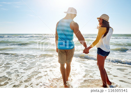 Couple, beach and holding hands with summer, holiday or vacation for love, support and romance in sun. Back of young people walking together and happy for anniversary, date or valentines day in ocean 116305541