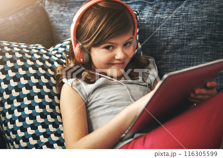 Tablet, headphones and portrait with girl on sofa in home living room for fun, learning on app or having fun. Kid, technology and happy child on couch, streaming movie or typing on social media Tablet, headphones and portrait with girl on sofa in home living room for fun, learning on app or having fun. Kid, technology and happy child on couch, streaming movie or typing on social media 116305599