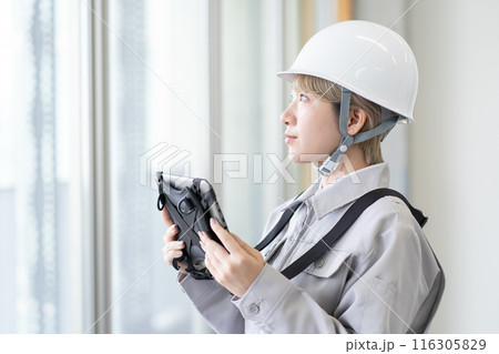 ヘルメットを被り作業服でタブレット端末を操作する金髪ショートヘアの若い女性作業員 116305829