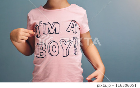Hands, child and point at text on shirt for gender identity, style and fashion model by blue background. Boy, toddler and kid with pink clothes for choice, learning and show print with affirmation 116306051