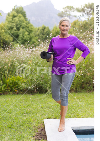 Outdoors, Caucasian senior female holding a yoga mat by a pool 116306346