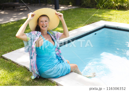 Outdoors, Caucasian senior woman holding a hat, laughing by pool Outdoors, Caucasian senior woman holding a hat, laughing by pool 116306352