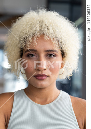 In modern office, biracial young woman with curly blonde hair standing alone 116306382