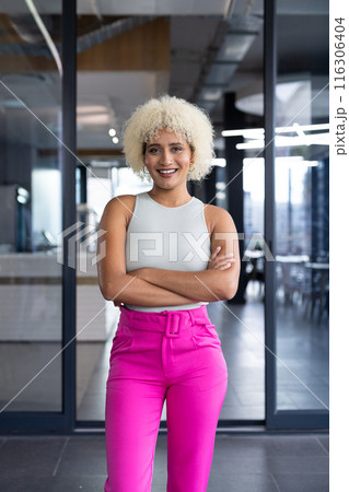 In modern office, young biracial woman standing, smiling at camera 116306404
