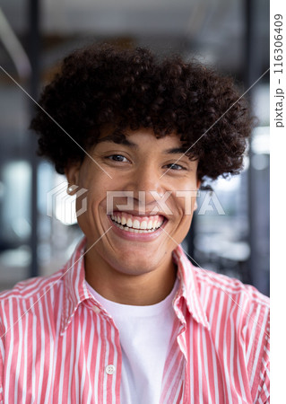 In modern office, biracial young male coworker wearing striped shirt, smiling 116306409