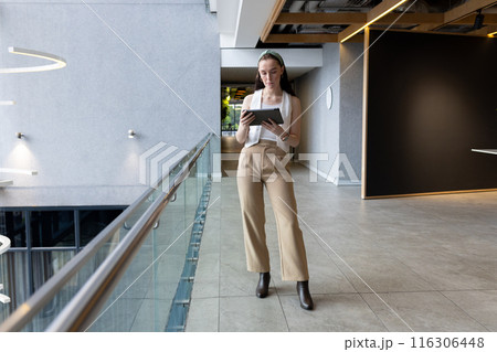 In modern office, young Caucasian female walking, reading tablet 116306448