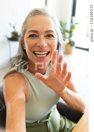 At home, mature Caucasian woman waving and smiling during video call 116306515