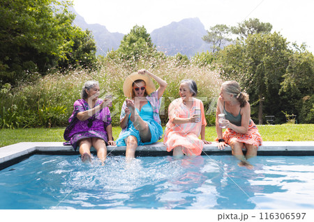 Outdoors, diverse senior female friends gathering by pool, laughing 116306597