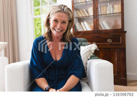 Caucasian senior woman in blue dress enjoying video call at home, smiling 116306702