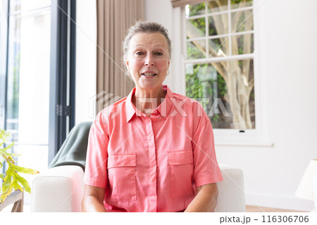Caucasian senior woman wearing pink shirt, smiling during video call at home 116306706