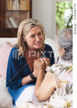 Diverse senior female friends sitting, talking at home with blue background 116306734