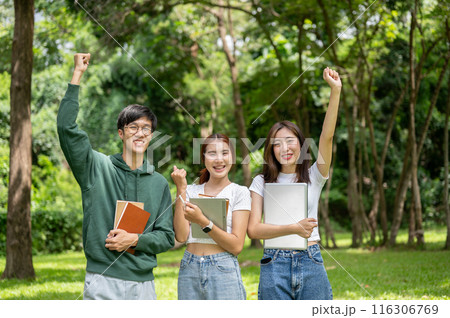 Cheerful young Asian college students smiling at the camera and showing their fists in the park. 116306769