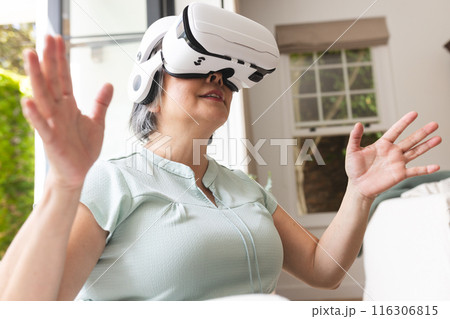 Senior Asian woman at home uses VR headset to explore a digital world 116306815