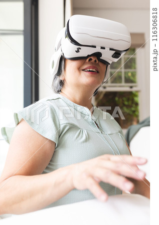 Asian senior female wearing virtual reality headset, sitting at home 116306818