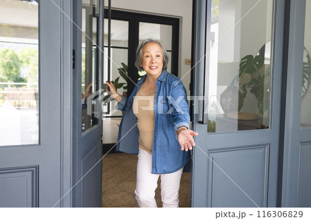 Asian senior female opening front door at home, inviting someone inside Asian senior female opening front door at home, inviting someone inside 116306829