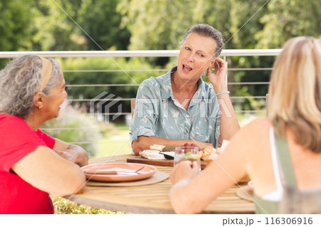 Diverse senior female friends sharing meal outdoors Diverse senior female friends sharing meal outdoors 116306916