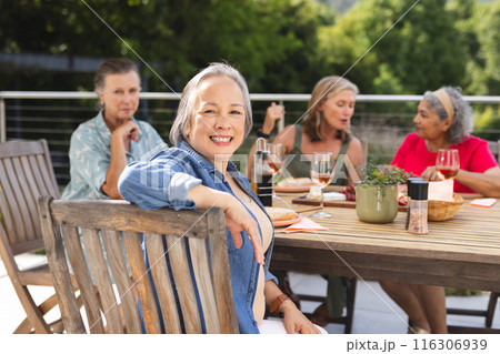 Diverse senior female friends enjoying meal outdoors, sharing stories 116306939
