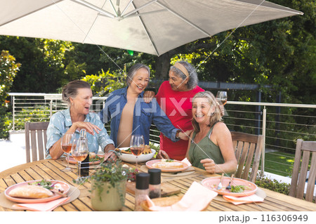 Diverse senior female friends enjoying lunch outdoors under umbrella Diverse senior female friends enjoying lunch outdoors under umbrella 116306949