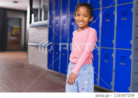 In school, young biracial girl is standing by blue lockers with copy space 116307209