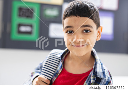 In school, young biracial boy with a striped backpack is smiling in the classroom In school, young biracial boy with a striped backpack is smiling in the classroom 116307232