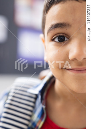 In school, young biracial boy with a striped shirt is smiling in the classroom, copy space 116307235