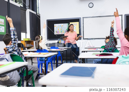 In school, a young biracial female teacher engages with eager young students in the classroom 116307243