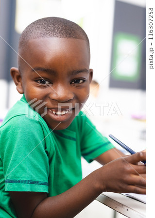 In school, young African American boy wearing a green shirt is writing in the classroom 116307258