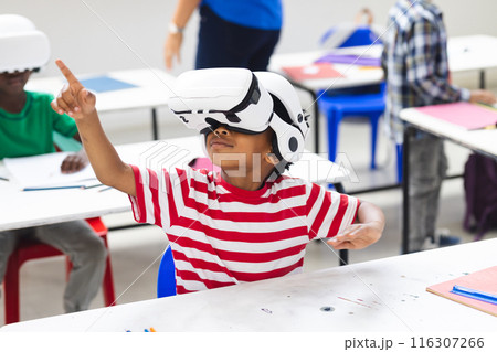 In school classroom, biracial boy wearing virtual reality headset pointing up 116307266