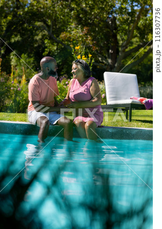 Outdoors, diverse senior friends holding hands by pool, chatting happily 116307736