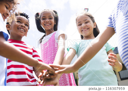 In school, diverse students are joining hands together outside 116307959