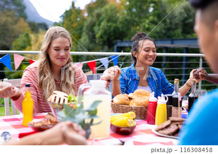 Happy diverse group of friends praying and having dinner at balcony with flags of usa 116308458