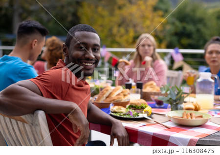 Portrait of happy diverse group of friends talking and having dinner at balcony with flags of usa Portrait of happy diverse group of friends talking and having dinner at balcony with flags of usa 116308475
