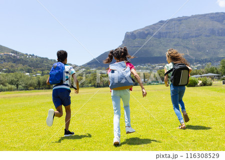 Three children are running joyfully across a grassy field on a sunny day 116308529