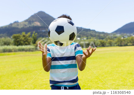 Biracial boy plays with a soccer ball outdoors, surrounded by greenery and mountains Biracial boy plays with a soccer ball outdoors, surrounded by greenery and mountains 116308540