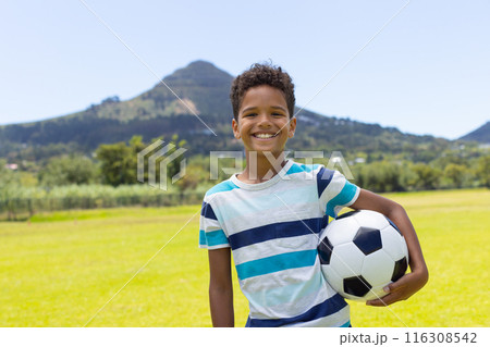 Biracial boy holding a soccer ball, smiling in a sunny outdoor setting Biracial boy holding a soccer ball, smiling in a sunny outdoor setting 116308542