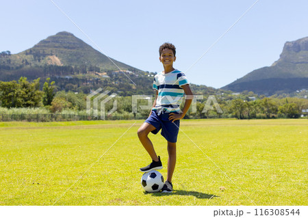 Biracial boy with a soccer ball stands confidently in a sunny park with copy space 116308544