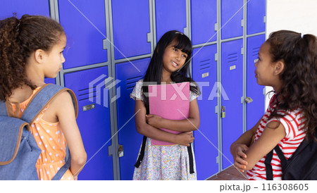 In school, three young biracial girls are talking by blue lockers outdoors In school, three young biracial girls are talking by blue lockers outdoors 116308605