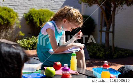 Caucasian girl with curly blonde hair is focused on reading outdoors in school 116308619
