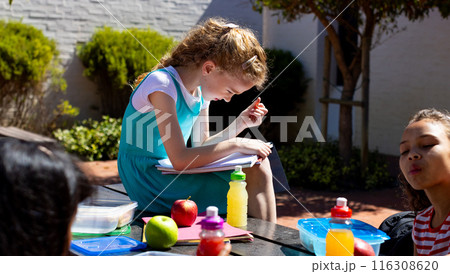 Caucasian girl focuses on her schoolwork outdoors, surrounded by peers 116308620