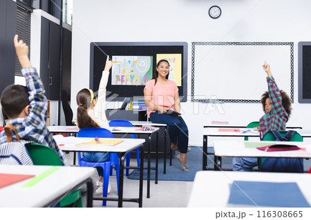In school, young biracial female teacher smiles at students raising hands in class In school, young biracial female teacher smiles at students raising hands in class 116308665