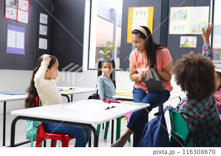 In school, young biracial female teacher engaging with diverse students in classroom 116308670