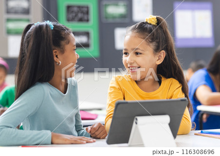 In school, biracial teacher guiding her diverse students during lesson in classroom 116308696