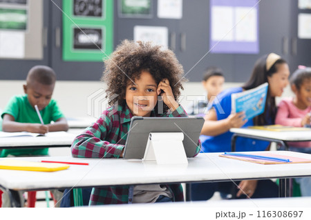 Young biracial girl with curly hair using tablet in classroom 116308697